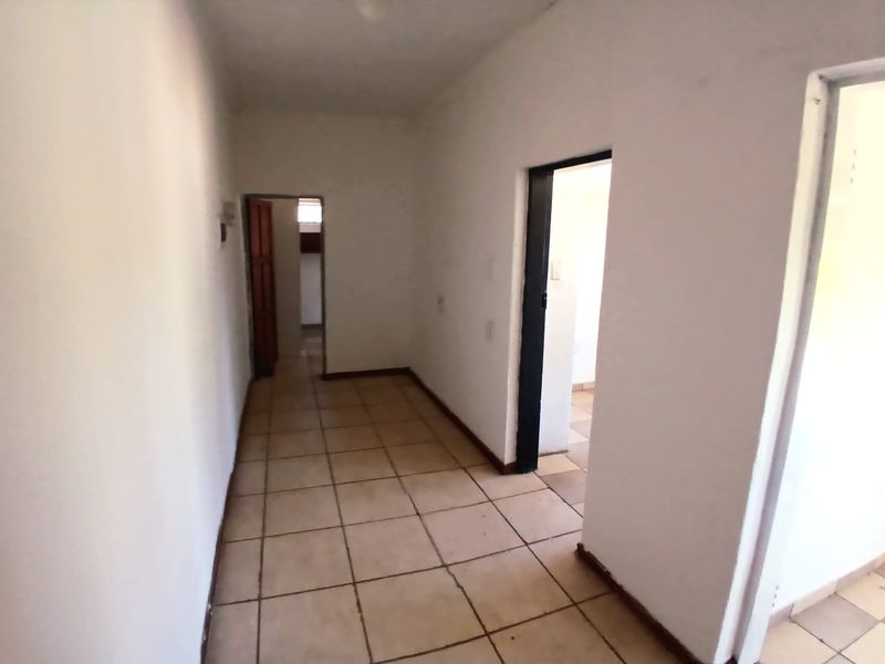 A vacant interior hallway featuring ceramic floor tiles and multiple doorways, showing signs of wear and requiring cosmetic updates.