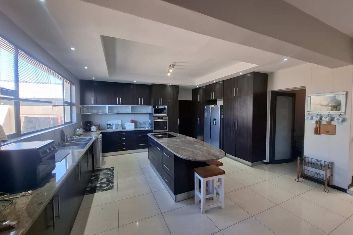 Modern kitchen featuring dark wood cabinetry, stone countertops, a central island with breakfast bar, and integrated appliances, finished with large format floor tiles.