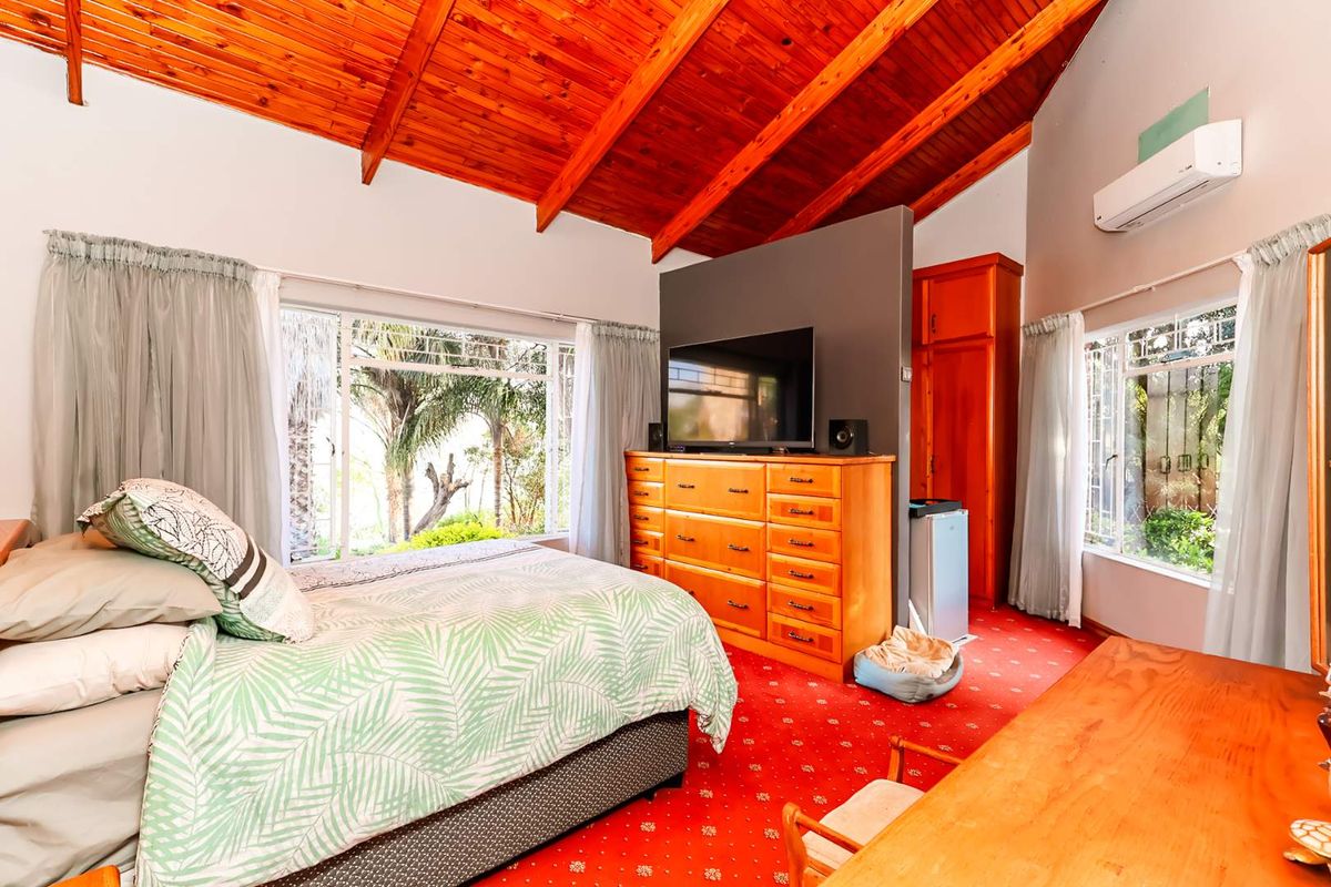 Spacious bedroom featuring a high exposed timber ceiling, large windows providing natural light, and a built-in cupboard for storage.