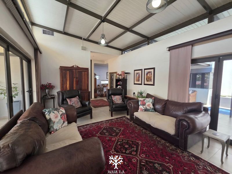 Spacious living room featuring an exposed beam ceiling, tiled flooring, and large sliding glass doors that provide ample natural light and access to the outdoors.
