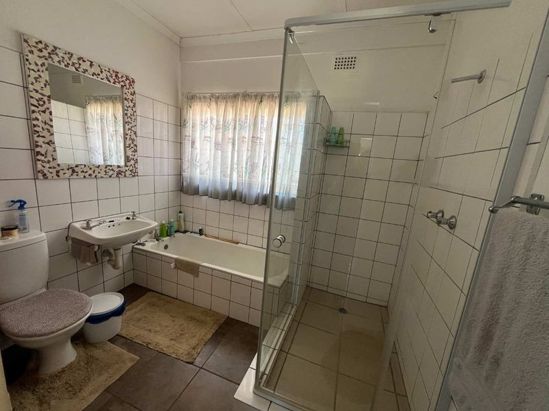 A functional bathroom featuring a built-in bathtub, separate glass-enclosed shower, and wall-mounted basin, finished with classic white wall tiling.