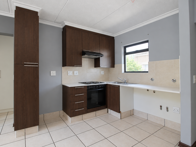 A functional kitchen featuring dark wood cabinetry, built-in oven and hob, tiled splashbacks, and tiled flooring, with space provided for additional under-counter appliances.