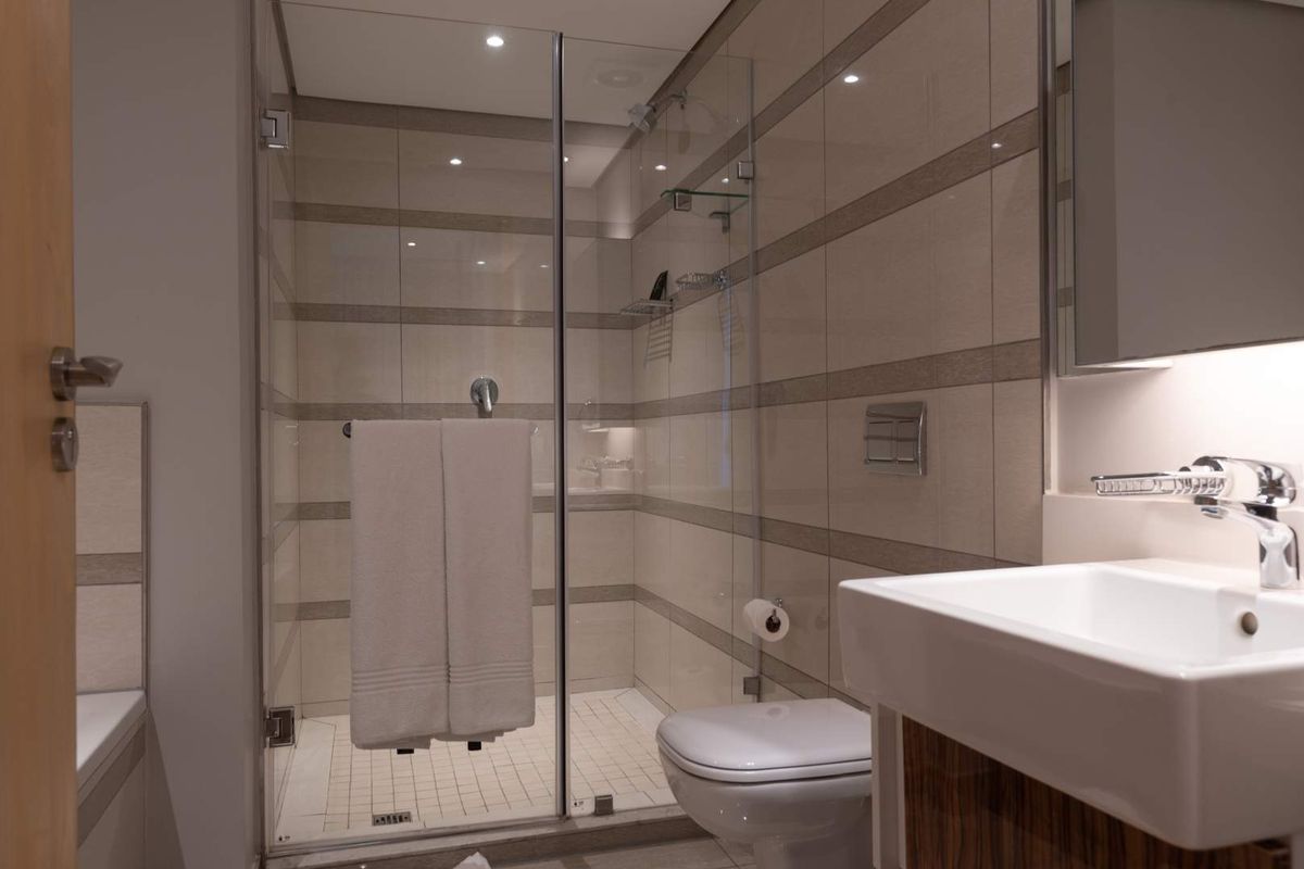 Modern bathroom featuring a glass-enclosed shower, wall-mounted toilet, and a sleek vanity basin with contemporary tiled finishes and recessed lighting.
