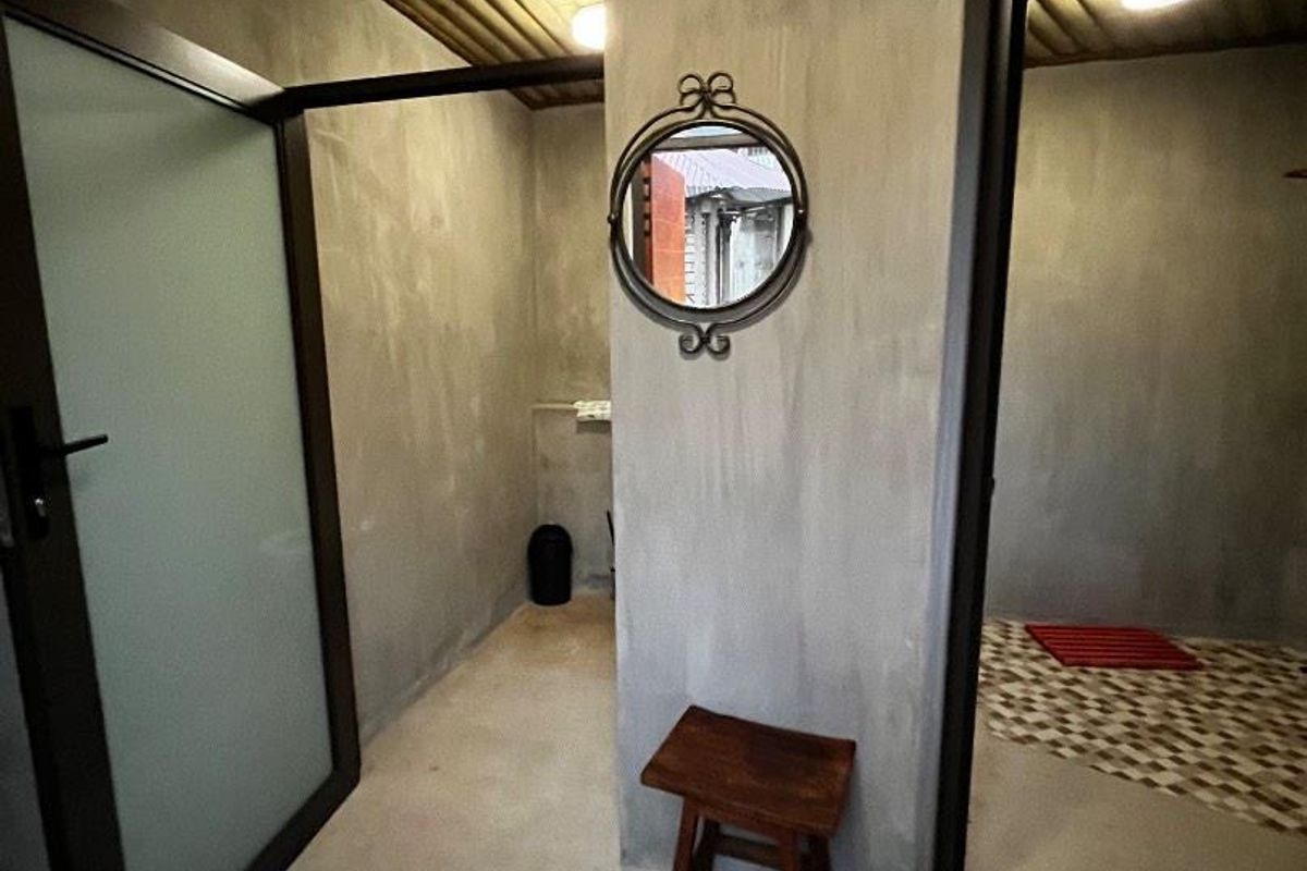 A minimalist bathroom area featuring concrete-finish walls, a timber slat ceiling, and a distinct transition to patterned floor tiles.