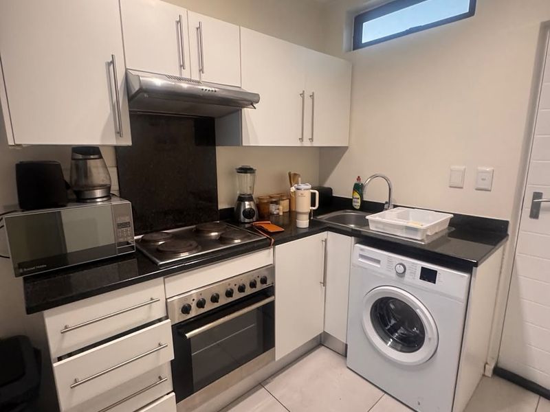 Compact kitchen featuring white cabinetry, black granite countertops, integrated oven and hob, and space for a washing machine.