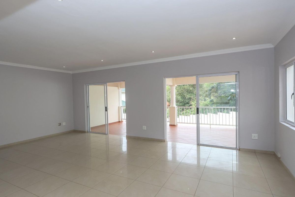 Spacious, light-filled living area featuring neutral tiled flooring, recessed downlighting, and dual sliding glass doors providing seamless access to the outdoor patio.