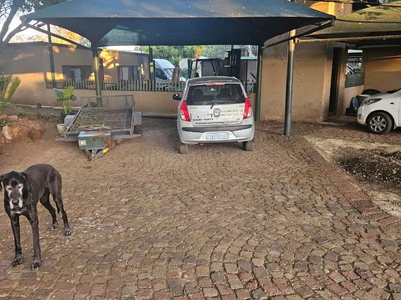 Outdoor parking area featuring a shade port structure and a cobblestone paved driveway.