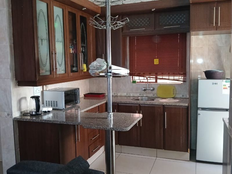 A functional kitchen featuring granite countertops, ample wooden cabinetry, and tiled flooring, offering a practical layout with integrated sink and prep space.