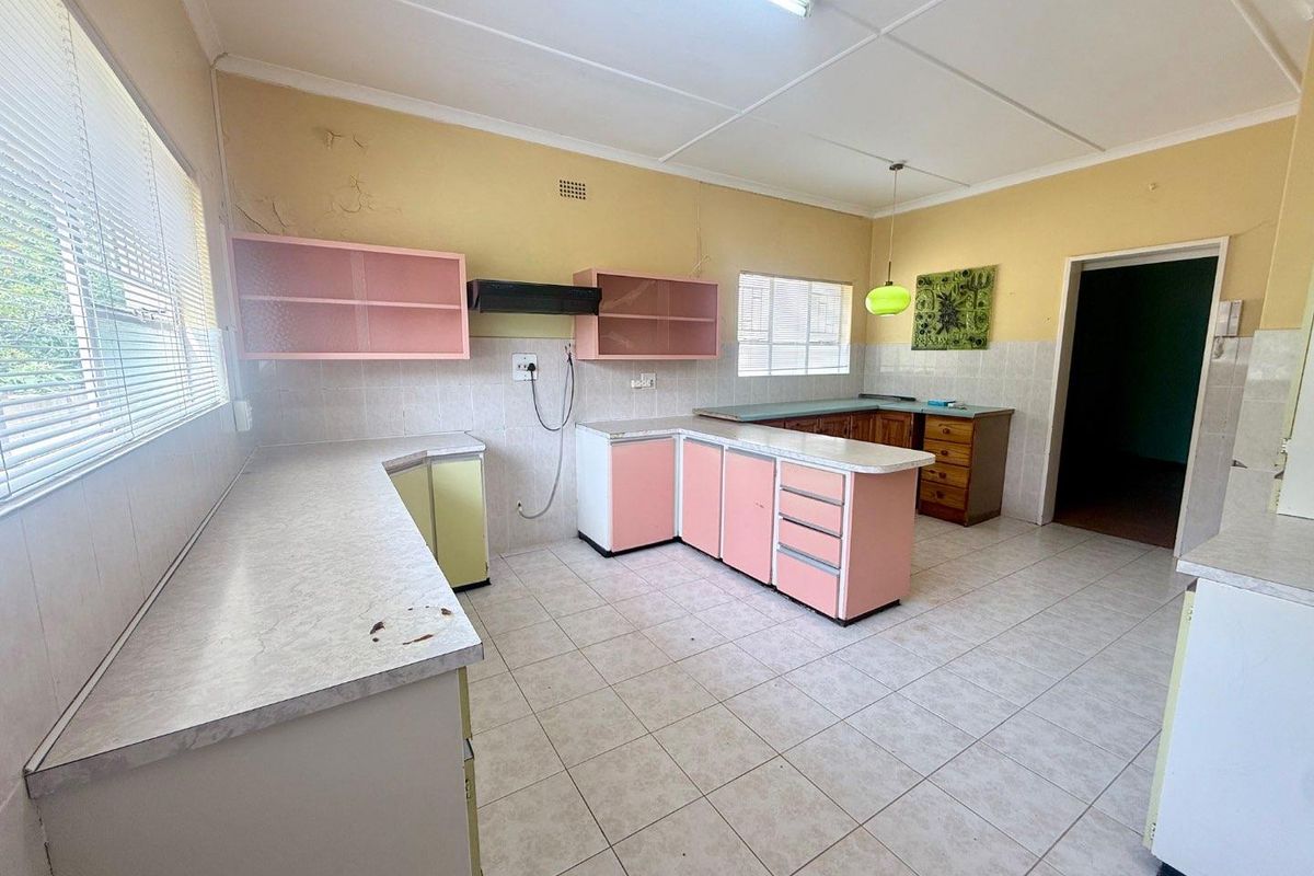 A spacious, empty kitchen featuring laminate countertops, built-in cabinetry, and tiled flooring, requiring cosmetic updates and wall repairs.