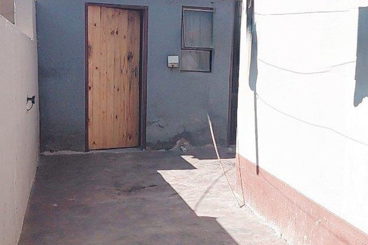 A narrow rear exterior passage featuring concrete paving, a timber door, and visible wear to the exterior wall finishes.