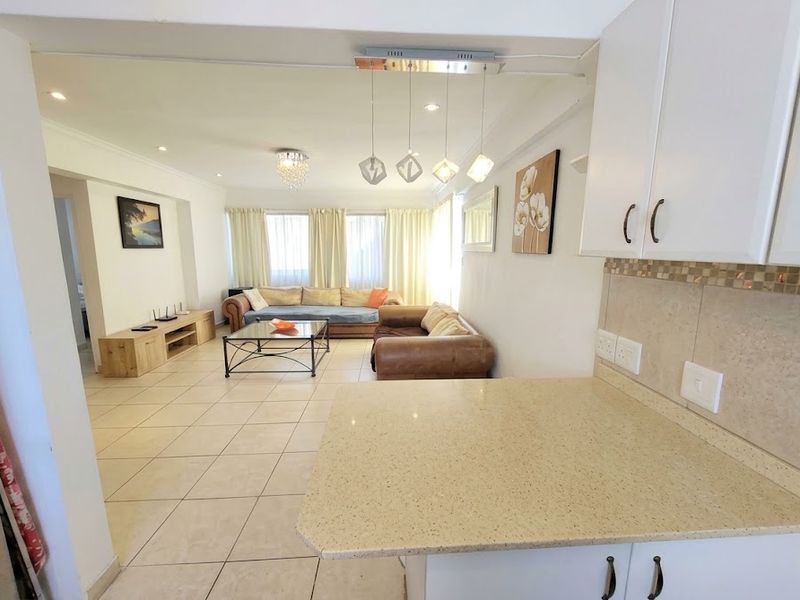 An open-plan living and kitchen area featuring tiled floors, modern cabinetry, stone countertops, and a mosaic backsplash, creating a bright and functional living space.