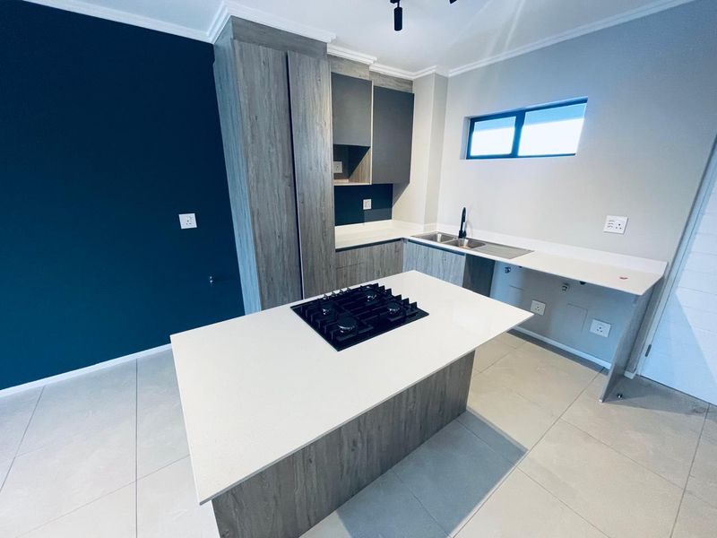 Modern kitchen featuring a central island with a gas hob, stone countertops, ample built-in cabinetry, and sleek tiled flooring in a contemporary finish.