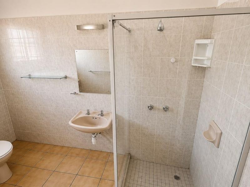 A functional bathroom featuring a shower enclosure, wall-mounted basin, and toilet with neutral wall tiling and floor tiles.