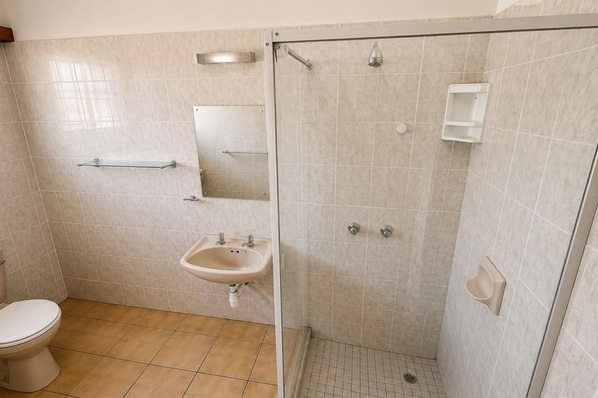 A functional bathroom featuring a shower enclosure, wall-mounted basin, and toilet with neutral wall tiling and floor tiles.