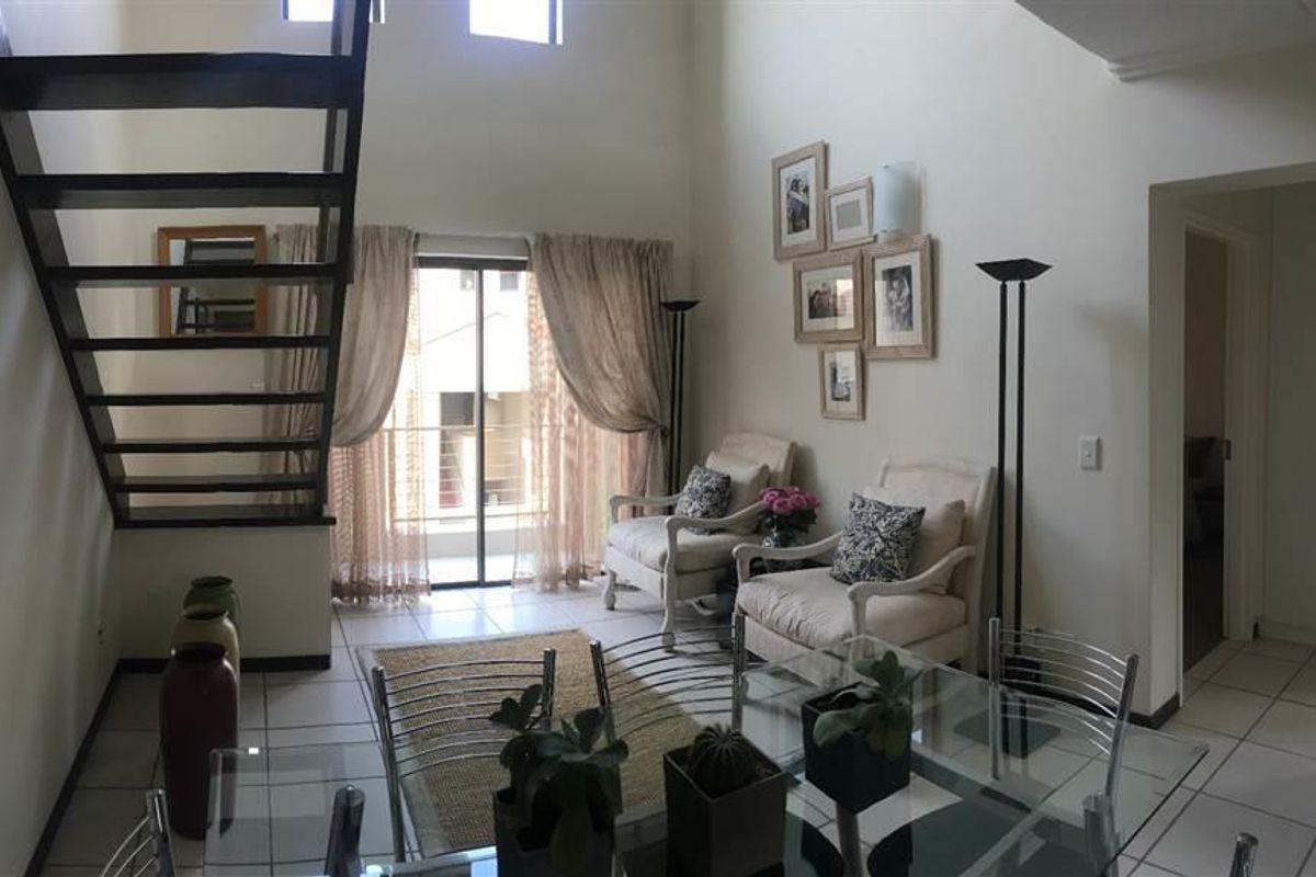 Open plan living area featuring double volume ceilings, tiled flooring, and a modern staircase leading to the upper level with access to a balcony.