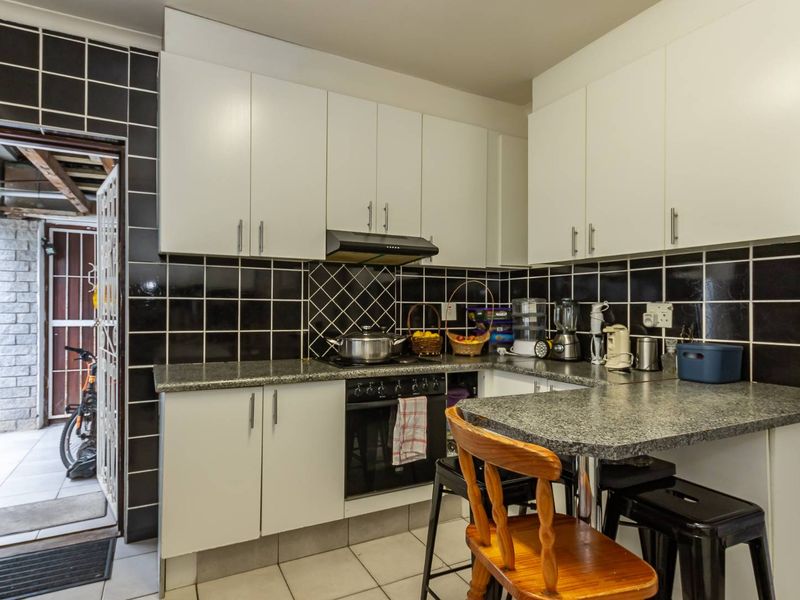 Compact kitchen featuring white cabinetry, granite countertops, a black tiled backsplash, built-in oven, extractor fan, and a small breakfast nook area.