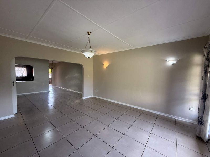 Spacious, empty living area featuring neutral tiled flooring, arched transitions to adjacent rooms, and a combination of ceiling and wall-mounted lighting.