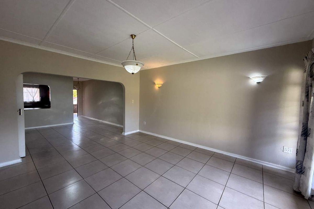 Spacious, empty living area featuring neutral tiled flooring, arched transitions to adjacent rooms, and a combination of ceiling and wall-mounted lighting.