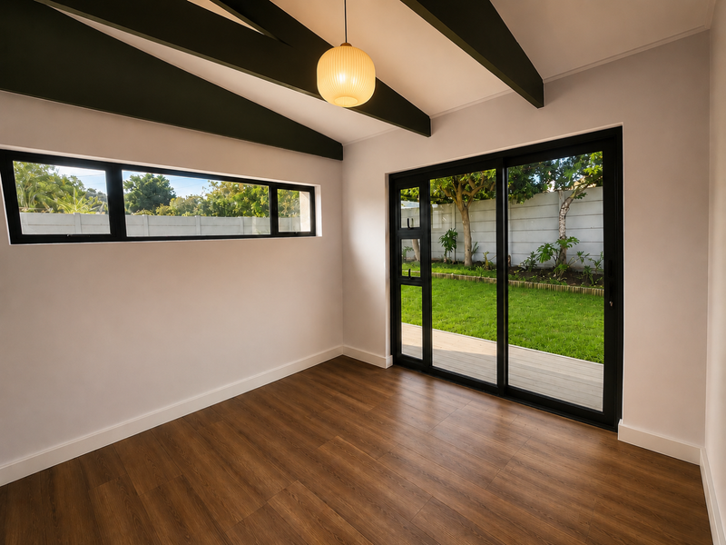 Bright, empty living area featuring exposed ceiling beams, modern laminate flooring, and large sliding glass doors providing direct access to the garden.