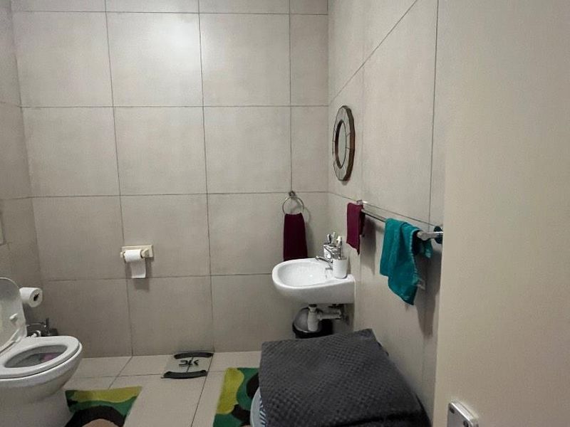 A functional bathroom featuring tiled walls and flooring, equipped with a wall-mounted basin and a standard toilet.