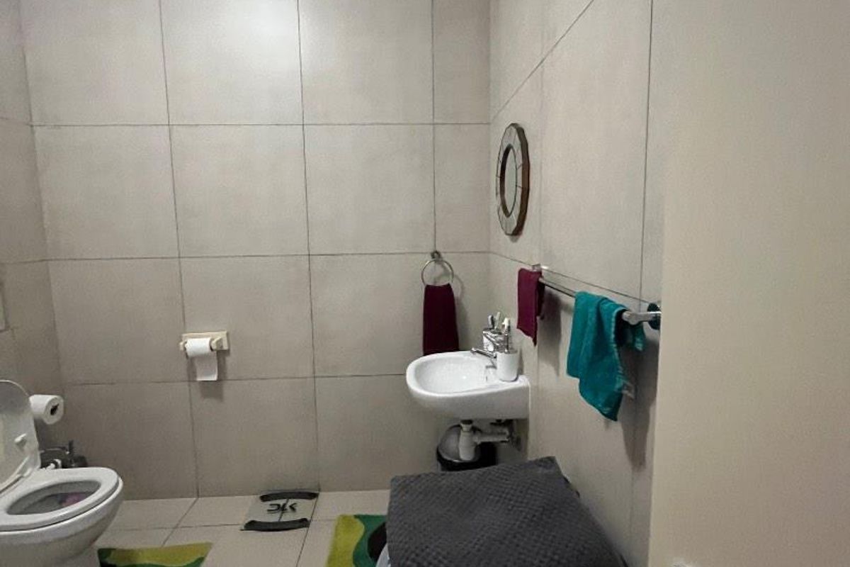 A functional bathroom featuring tiled walls and flooring, equipped with a wall-mounted basin and a standard toilet.