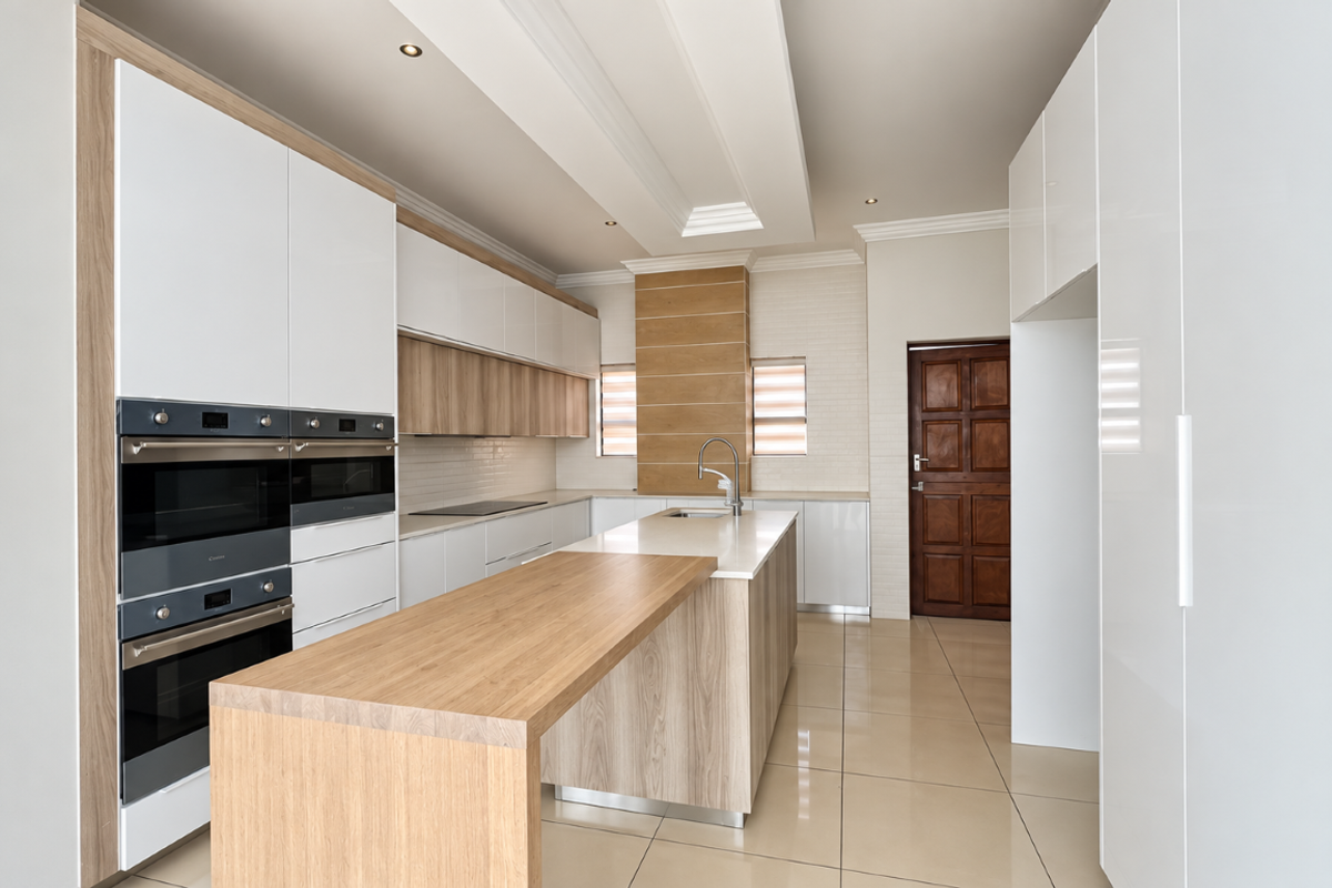 Modern kitchen featuring sleek white and wood-grain cabinetry, a central island with stone countertops, built-in double ovens, and polished tile flooring.