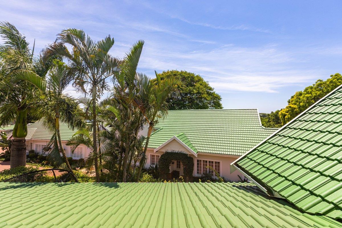 An elevated view overlooking the green tiled roof of the property, surrounded by lush palm trees and landscaped garden areas.