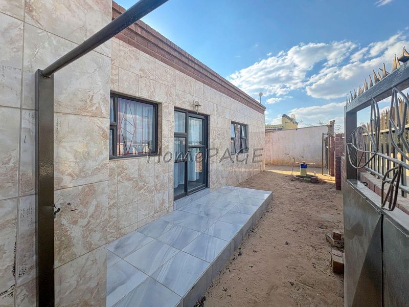 Rear exterior view of the property featuring a tiled facade, a small tiled patio area, and aluminium framed windows and doors.