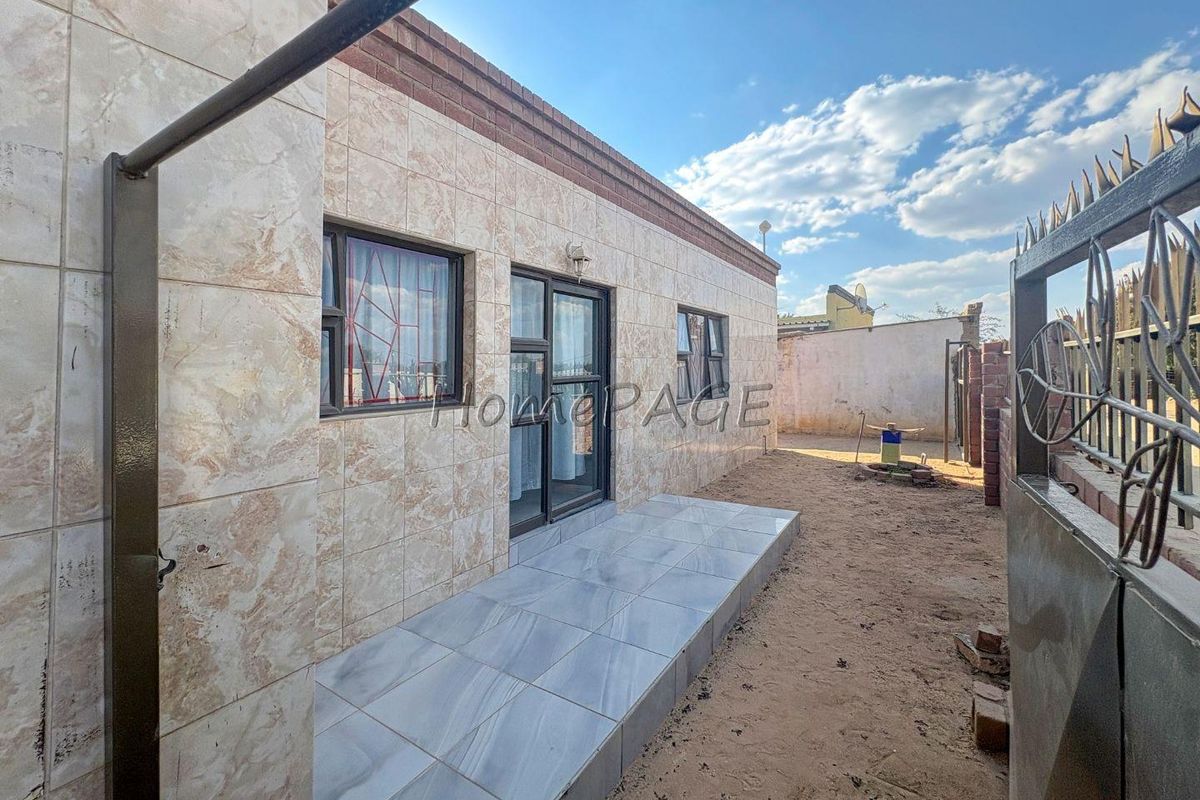 Rear exterior view of the property featuring a tiled facade, a small tiled patio area, and aluminium framed windows and doors.