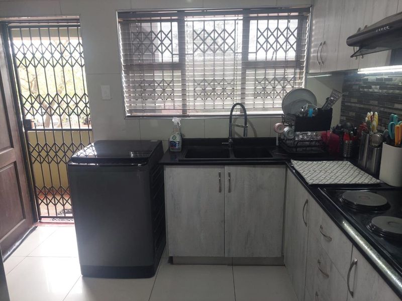 Functional kitchen featuring stone countertops, built-in cabinetry, a hob with extractor fan, and direct access to an exterior security gate.