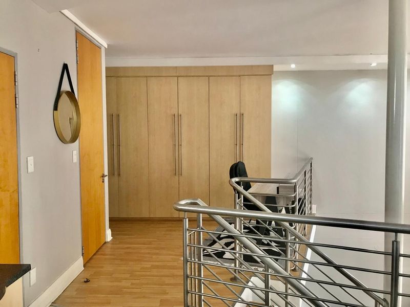 A landing area featuring built-in wooden cupboards, laminate flooring, and a modern stainless steel balustrade overlooking the lower level.