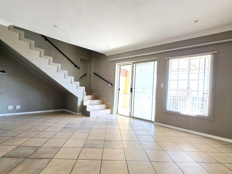 Spacious open-plan living area featuring tiled flooring, a staircase, and sliding glass doors leading to an outdoor space.