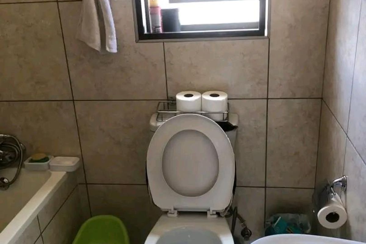 A functional bathroom featuring floor-to-ceiling wall tiles, a standard toilet, and a bathtub with integrated shower fixtures.