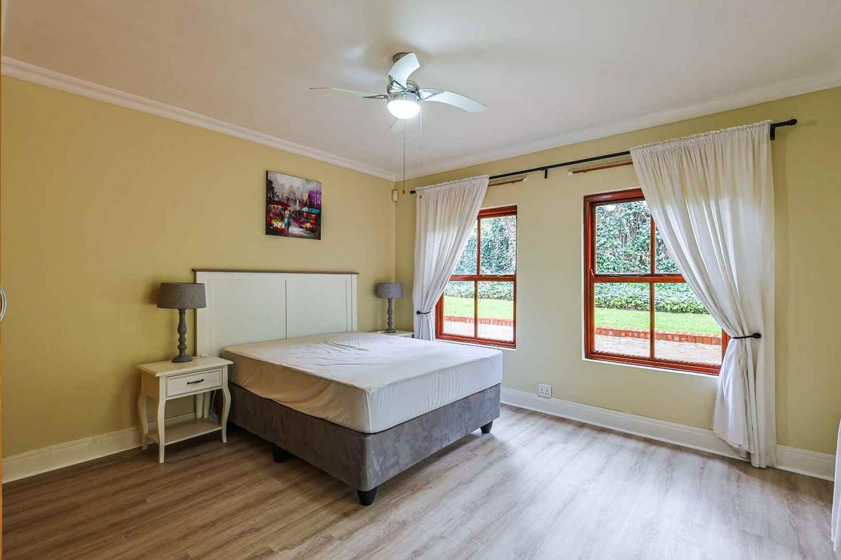 A well-maintained bedroom featuring light wood-look flooring, a ceiling fan, and large windows that provide natural light and views of the garden.