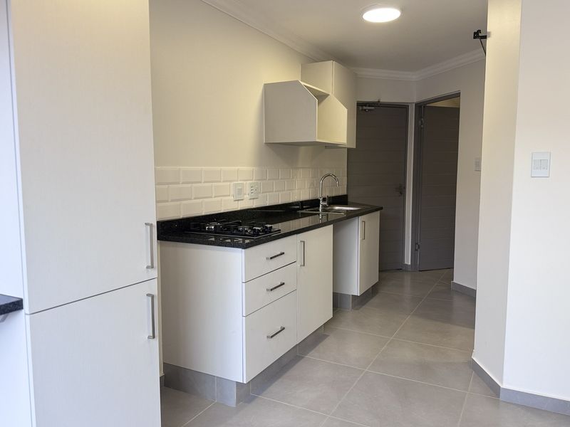 Modern kitchen featuring white cabinetry, granite countertops, subway tile backsplash, gas hob, and tiled flooring in a clean, minimalist layout.