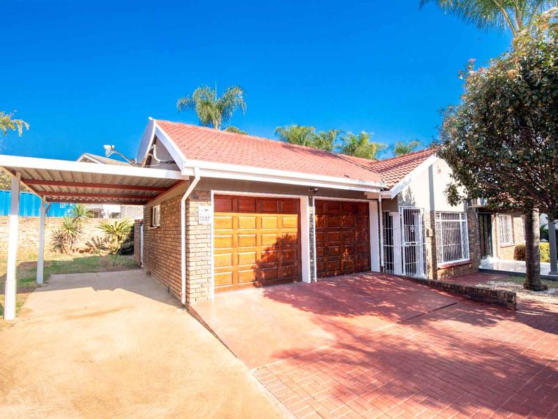 Front view of the property featuring a double garage, attached carport, and paved driveway with established garden surroundings.
