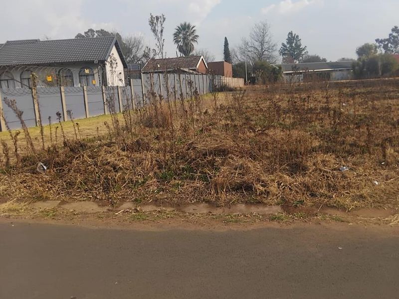 A vacant residential plot featuring perimeter fencing and direct access to a paved road, situated in an established neighborhood.