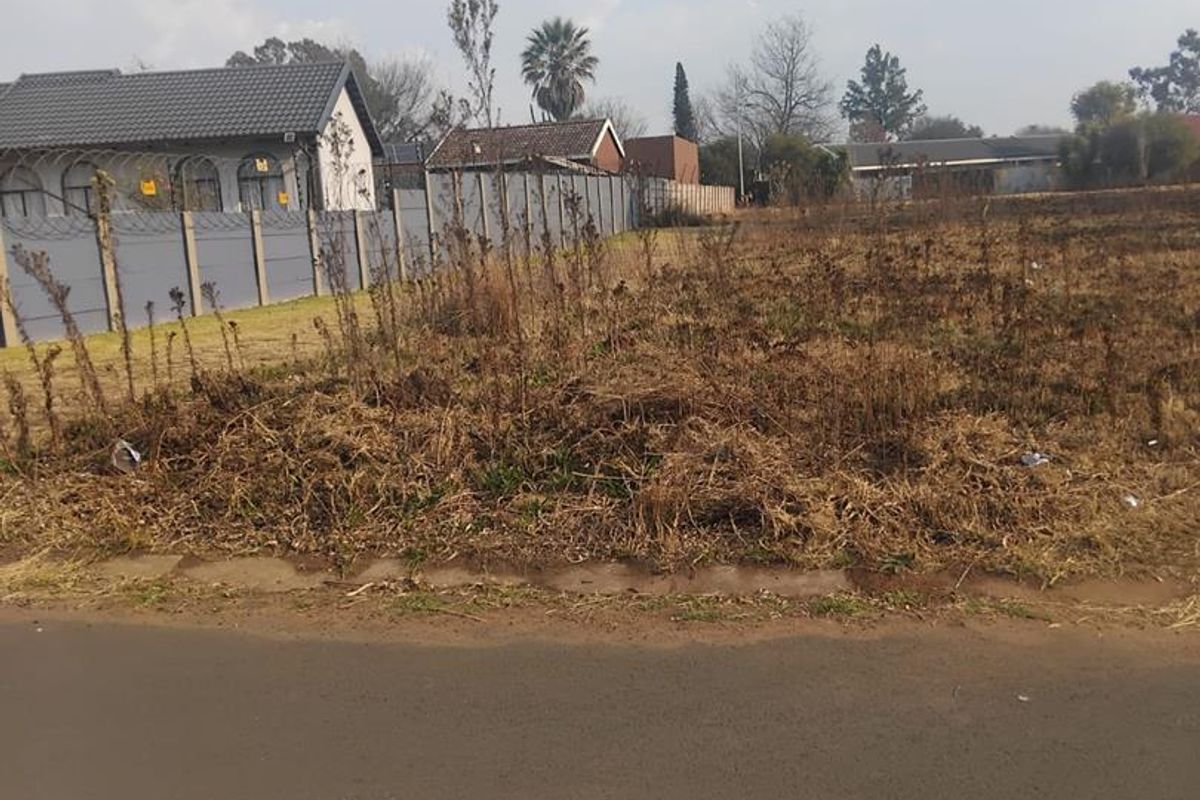 A vacant residential plot featuring perimeter fencing and direct access to a paved road, situated in an established neighborhood.