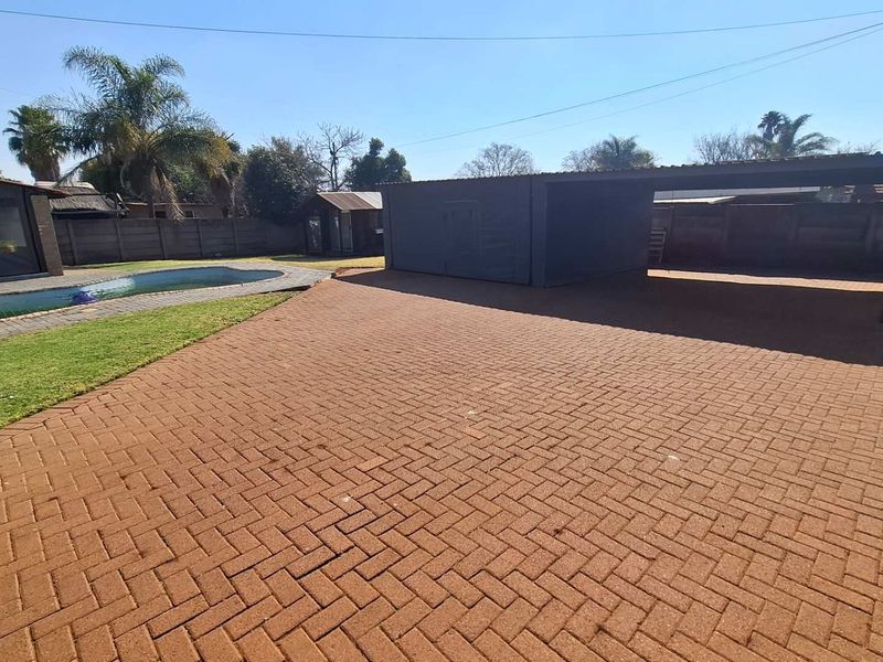 Spacious rear yard featuring a paved driveway, a covered carport, a swimming pool, and a well-maintained lawn area enclosed by boundary walls.