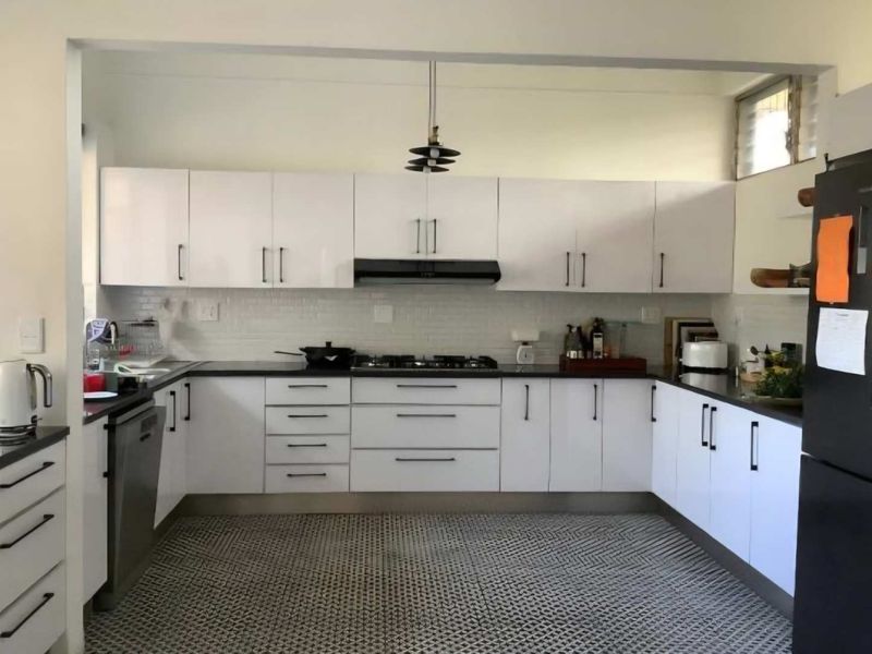 A modern U-shaped kitchen featuring white cabinetry, dark stone countertops, a gas hob with extractor fan, and a patterned tiled floor.