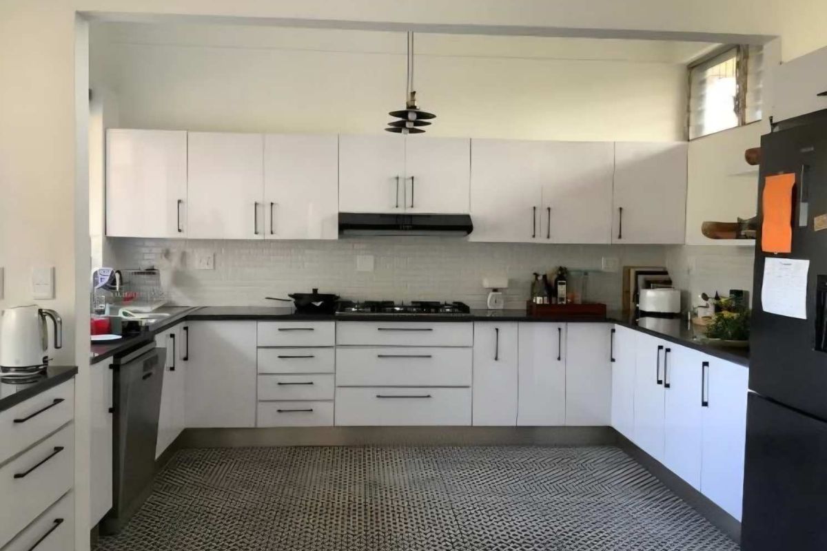 A modern U-shaped kitchen featuring white cabinetry, dark stone countertops, a gas hob with extractor fan, and a patterned tiled floor.