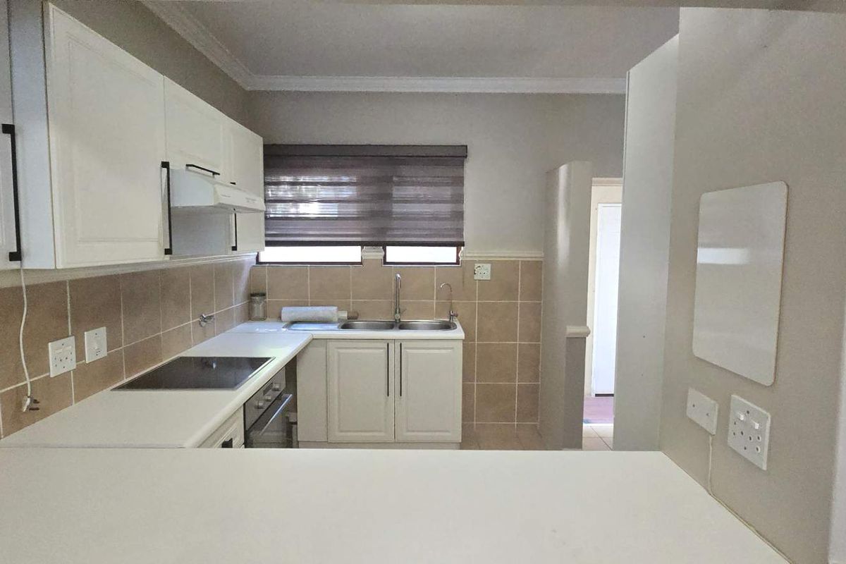 A clean and functional kitchen featuring white cabinetry, a double sink, built-in oven, electric hob, and neutral tiled backsplash.