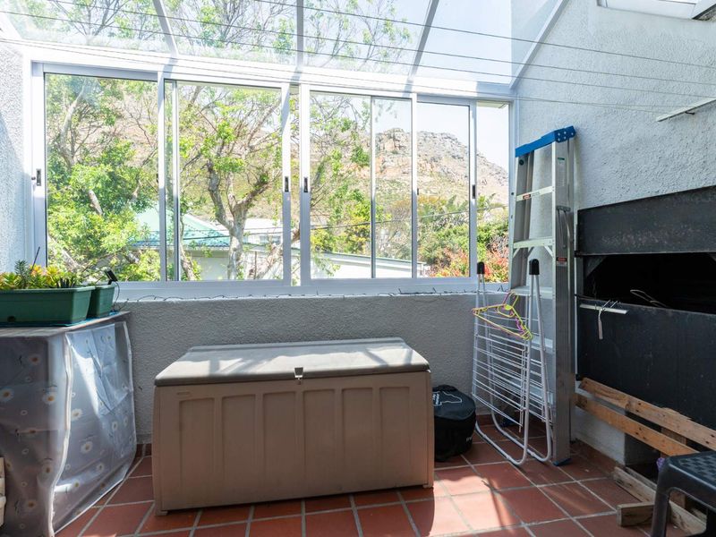 Enclosed patio area featuring a built-in braai, tiled flooring, and large sliding windows with views of the surrounding greenery and mountain.
