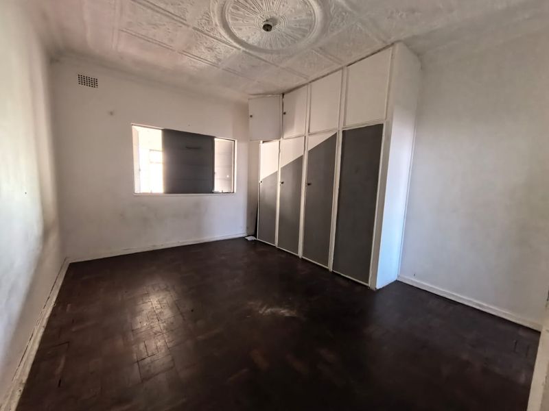 An empty bedroom featuring original parquet flooring, a decorative pressed metal ceiling with a central rose, and built-in storage cupboards.