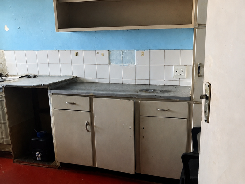 A dated kitchen area featuring basic built-in cabinetry, a tiled backsplash, and an integrated extractor fan, requiring significant renovation and cosmetic updates.