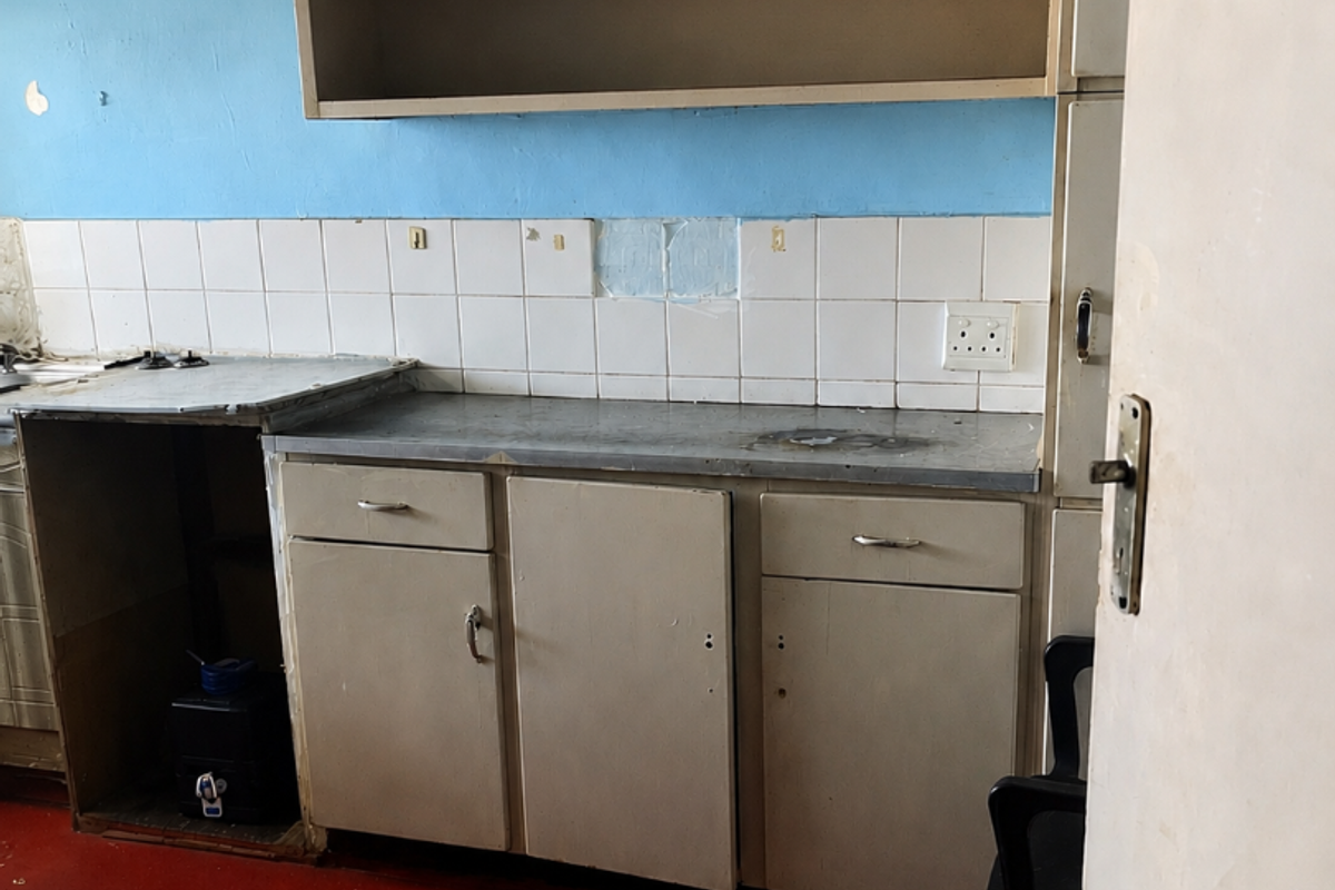 A dated kitchen area featuring basic built-in cabinetry, a tiled backsplash, and an integrated extractor fan, requiring significant renovation and cosmetic updates.