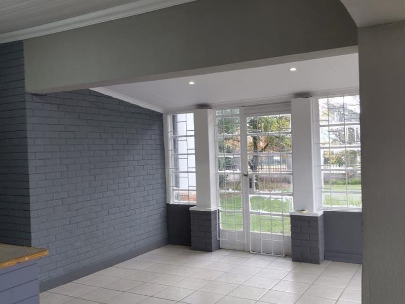 A bright, enclosed patio area featuring tiled flooring, painted brick walls, and glass-paned french doors leading to the garden.