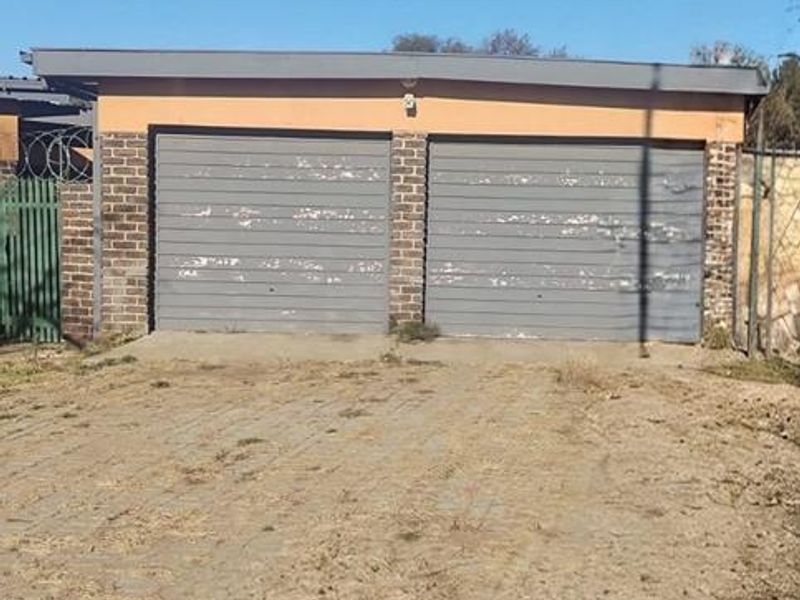 A detached double garage featuring a brick facade and paved driveway, showing signs of exterior wear and maintenance requirements.