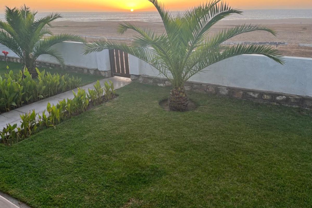 A scenic view of the ocean at sunset, featuring a well-maintained garden, stone boundary wall, and direct access to the beach area.