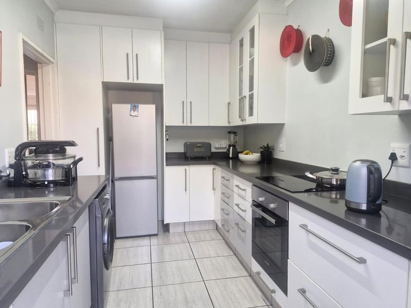 A functional kitchen featuring white cabinetry, dark stone countertops, integrated oven and cooktop, and tiled flooring with a dedicated laundry appliance space.